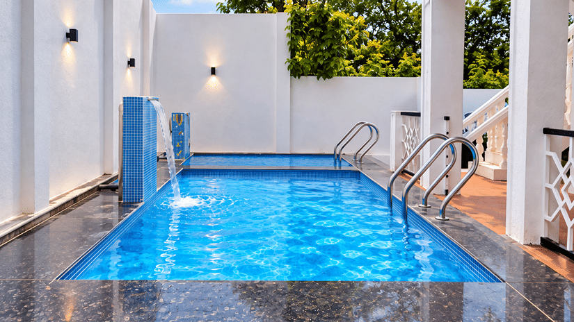 Private swimming pool at MGM Whispering Nest, with blue mosaic tiling, a stone deck, white pergola seating and a fountain spout along the poolside wall.
