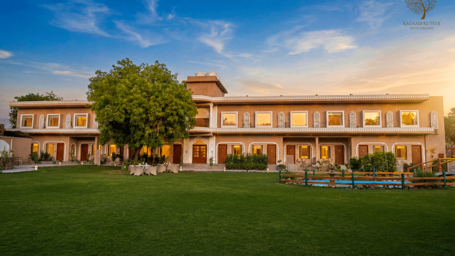 Front view of the property with a manicured lawn and warm golden hour sky at Kadamb Kuteer, Vrindavan.