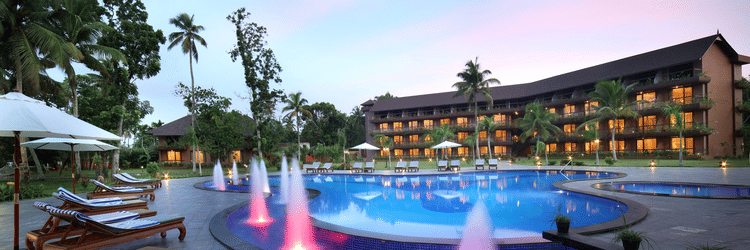 Mini fountains next to the pool with a backdrop of the facade of Uday Backwater Resort under a colourful sky