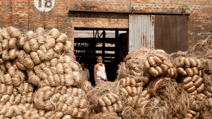 A person sitting among large piles of coiled natural fibre outside a brick building.