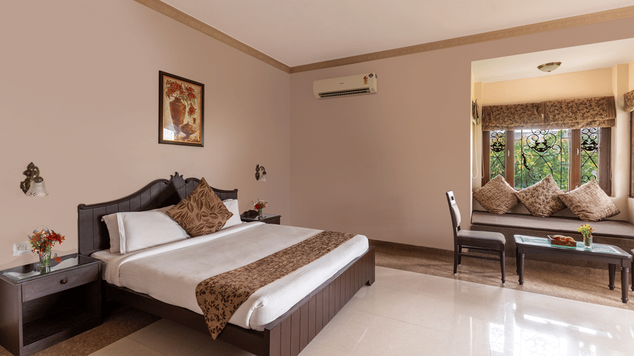 A well-lit guest room with a double bed and window alcove seating at Mewar Mansion Villa By Amantra, Udaipur.