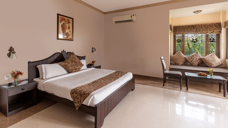 A well-lit guest room with a double bed and window alcove seating at Mewar Mansion Villa By Amantra, Udaipur.