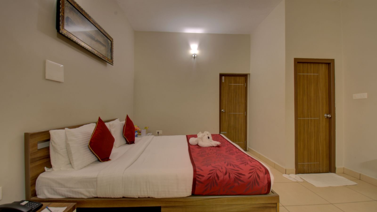 A bedroom with a huge bed, side table, wooden doors and a wall art | Superior Room | Woodstock Resorts, Coorg