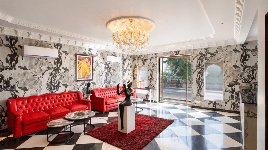 Opulent hotel lounge interior with red velvet sofa, chandelier, and monochrome patterned walls.