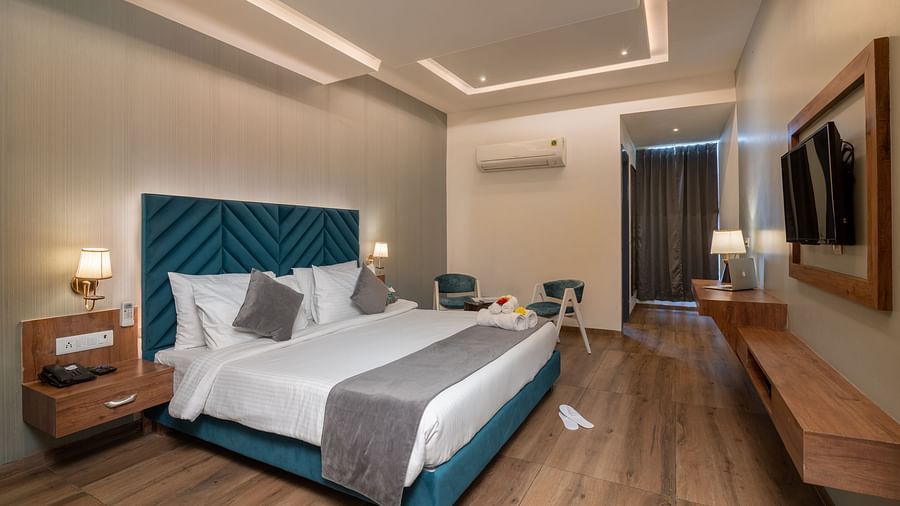 A premium room at DLS Ganga Bliss, Haridwar with a bed, bed side tables, lamps, a flat screen TV, two chairs and a coffee table
