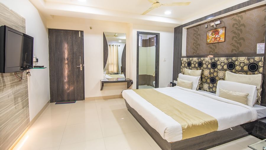 A room featuring a wooden bed, a TV, a wall painting and a wardrobe - Hotel Morya, Bhopal