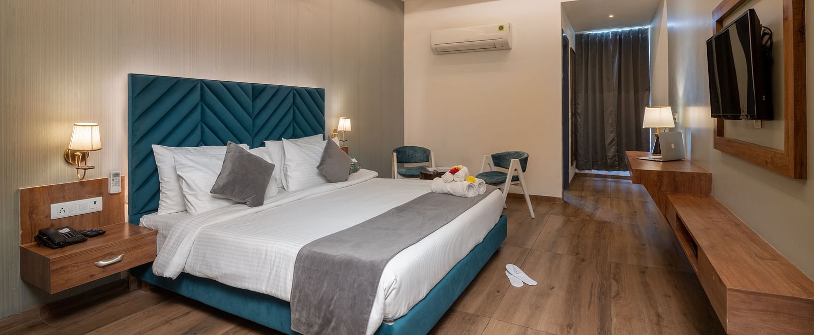A premium room at DLS Ganga Bliss, Haridwar with a bed, bed side tables, lamps, a flat screen TV, two chairs and a coffee table