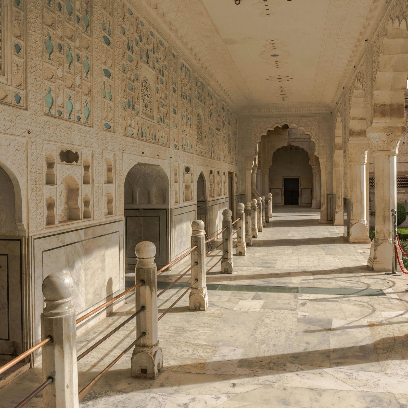 Long corridor with arches and columns inside a historic building, featuring carved details and an open walkway.