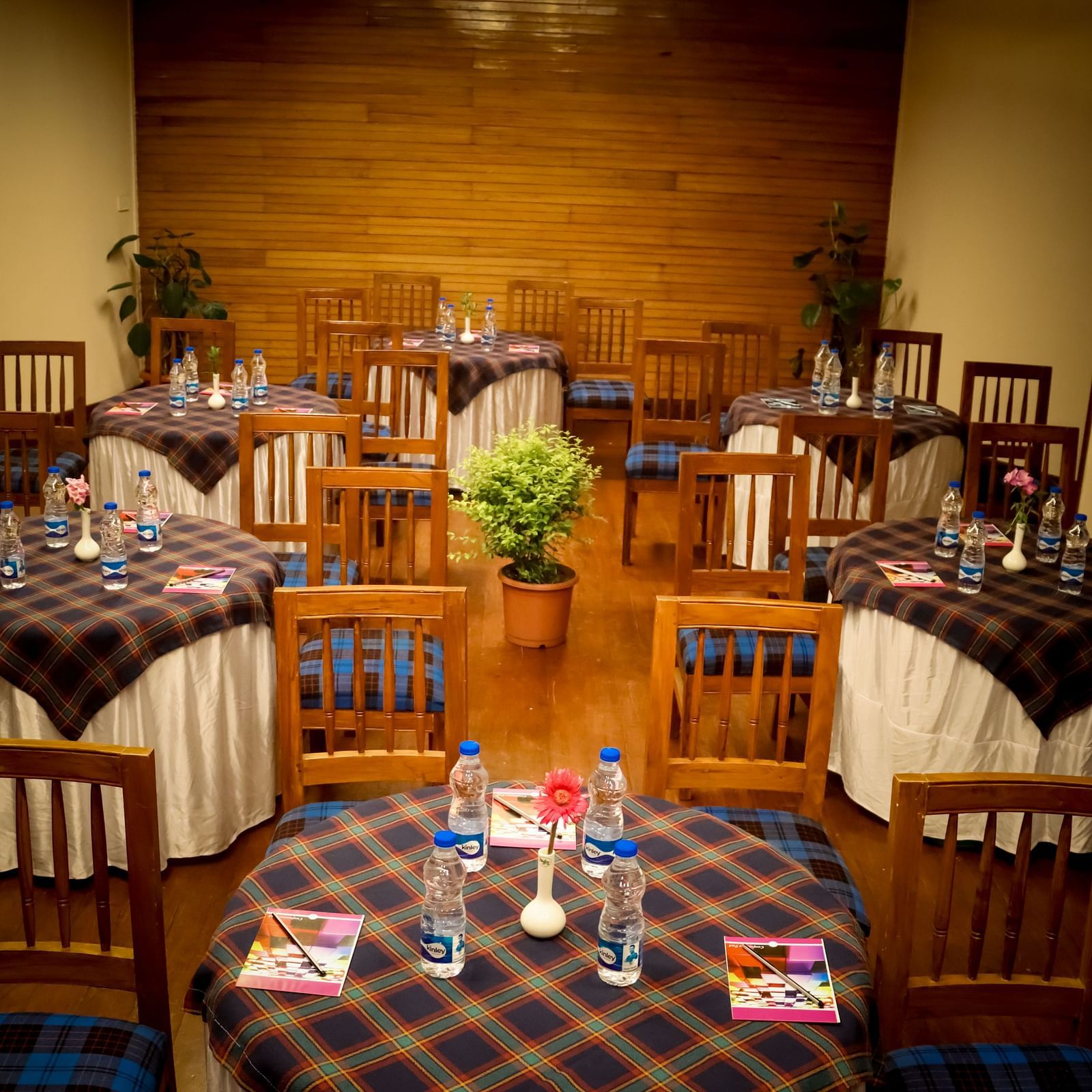 Banquet Hall at Cedar Inn, Darjeeling set for a meeting with water bottles, notepads, and chairs arranged around tartan-covered tables.