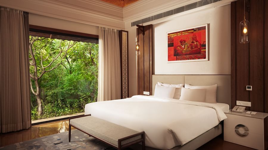 A spacious bedroom at The Ananta Udaipur with a king-sized bed, large windows overlooking a lush garden, and a wooden headboard.