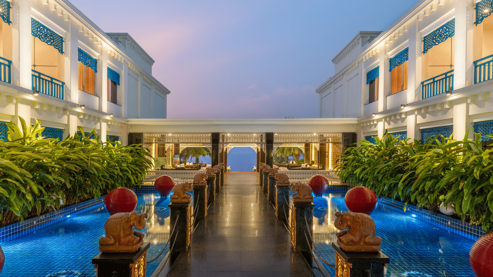 Courtyard lit at dusk with reflecting pools, carved elephant statues, red lanterns and lit building wings at MAYFAIR Palm Beach Resort, Gopalpur-on-Sea.