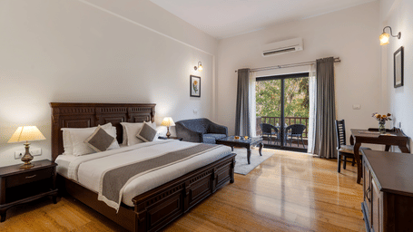 Full view of the Hill View Suite With Balcony featuring a wooden flooring and a double bed in the centre, along with a seating area beside it.