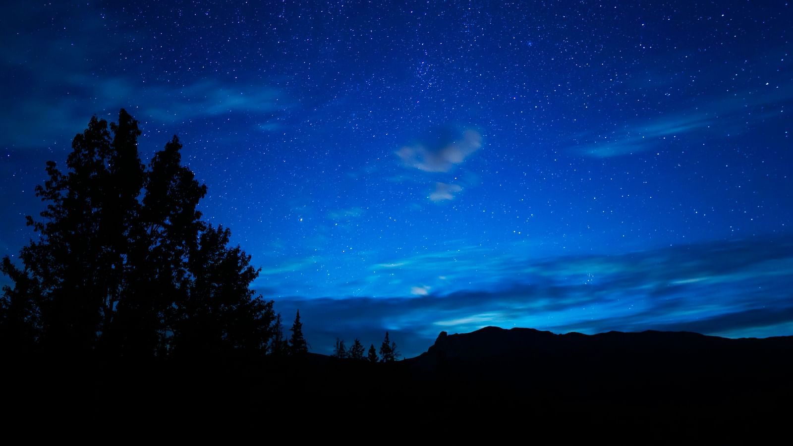 an overview of the night sky with patches of clouds on it and a tree on the side