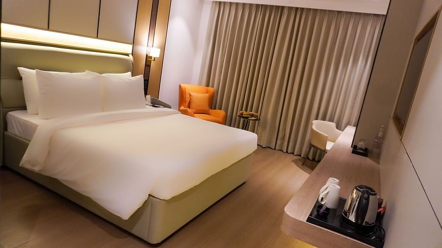 A bright hotel Deluxe room showcases a king-sized bed with crisp white bedding, bedside tables, and a window with sheer and blackout curtains - The Orchid Hotel, Chandigarh