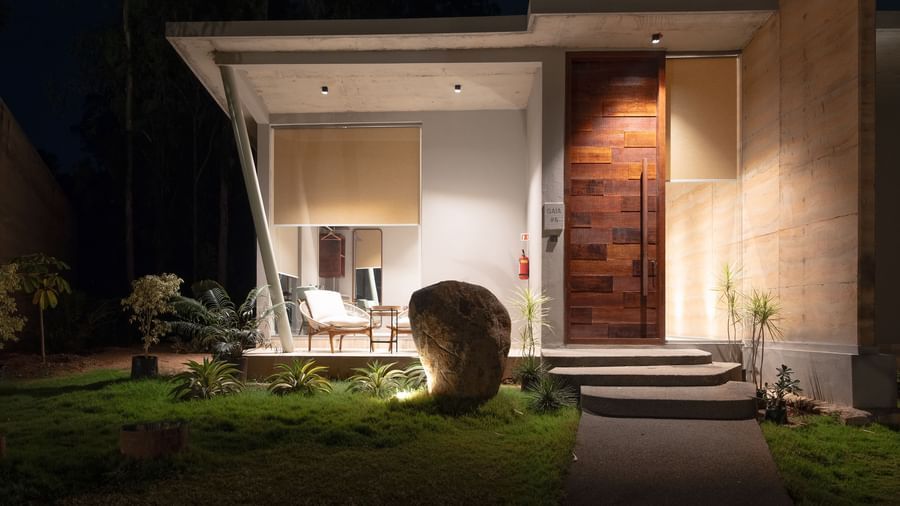 An illuminated exterior view of a modern house at night, highlighting the entrance and warm interior lighting | Gaia Studio | RD's Nature Retreat, Bangalore