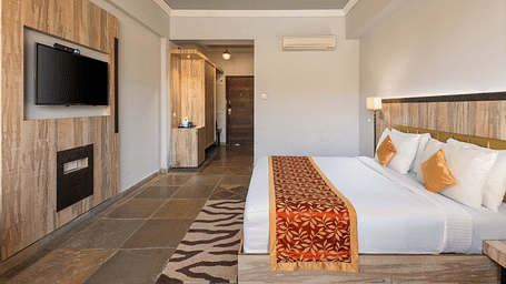 A hotel room with a bed, TV, a door leading to another room, and a patterned rug on the floor - Via Lakhela Resort & Spa, Kumbhalgarh