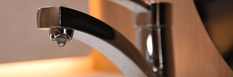 A modern chrome faucet with a single water droplet suspended from the spout.