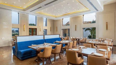 The restaurant at EsthereaRaj Leela, Ranakpur, featuring large windows, set tables, and a central blue upholstered booth partition.