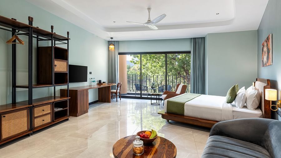 Club Suite with Valley View Sitout furnished with a plush sofa, a king size bed, and a TV, with a view of the outdoors through sliding glass doors at The Qualia Resort Club & Brewery, Udaipur.