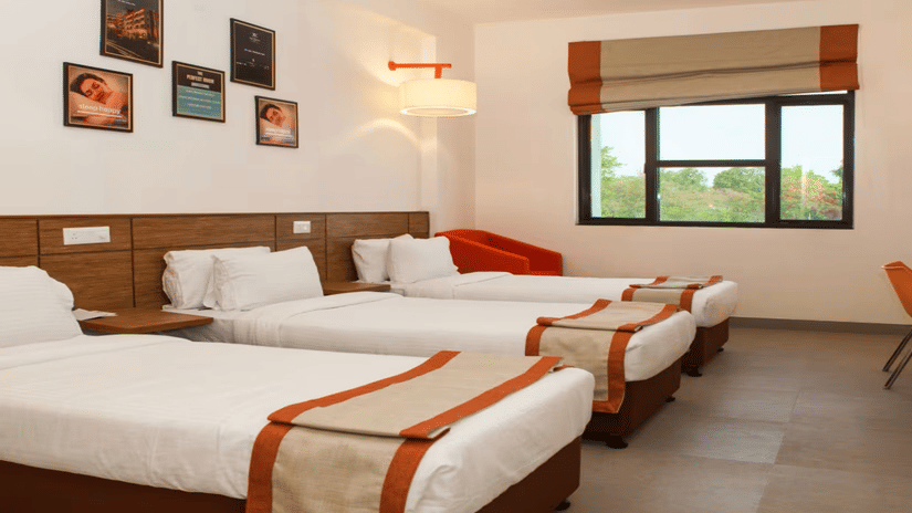 A spacious comfy room with 3 plushy bed, posters on wall, an open window at Max Hotel Prayagraj.