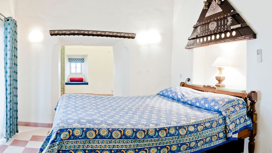 A bedroom with a bed, a decorative wall hanging, and a doorway leading to another room in Tijara Fort-Palace - 19th Century, Alwar.