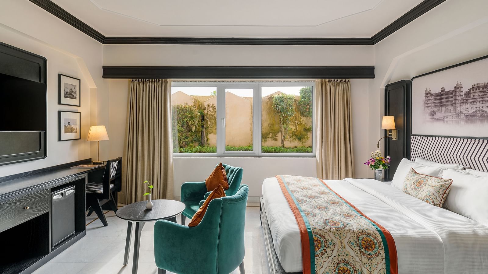 a spacious room featuring a king size bed, two comfortable green armchairs, with a table lamps and a window - Hotel Rajdarshan, Udaipur.