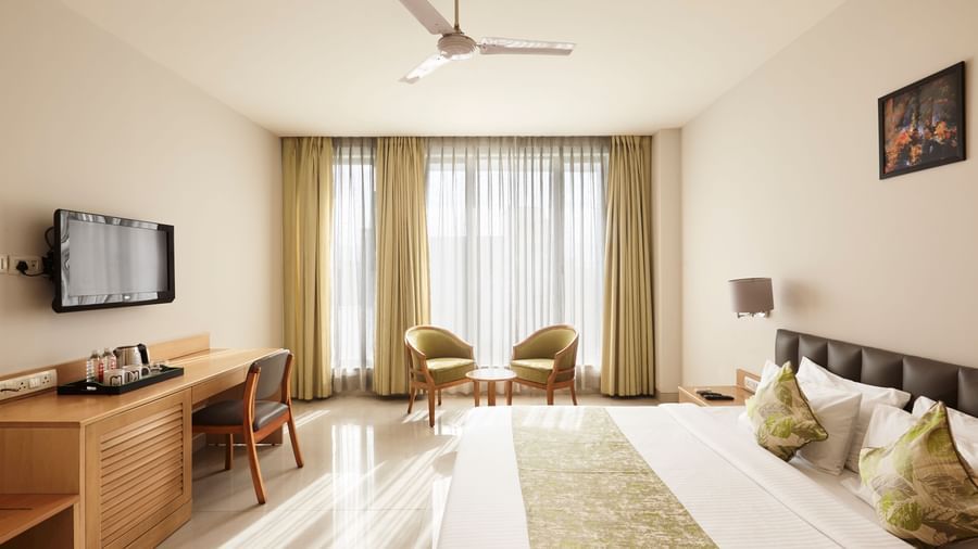 A wide-angle view of a modern hotel room at Monday Hotels Mahape, Navi Mumbai, with the bed and a view into the bathroom.
