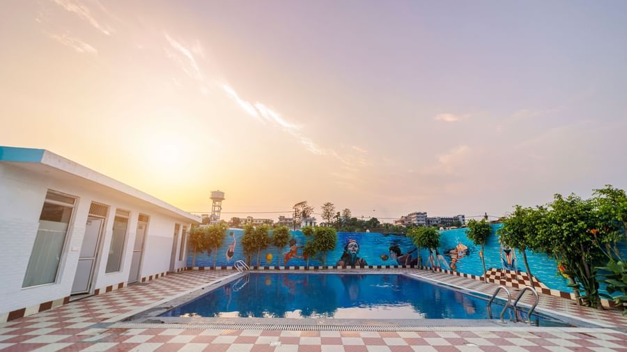 Swimming pool at Inde Reva Resorts Rishhikesh surrounded by poolside seating and tiled deck at sunset.