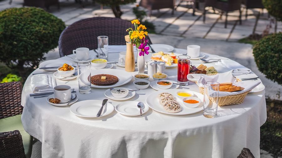  An outdoor dining table adorned with a white tablecloth featuring a variety of food served at The Claridges Nabha Residence