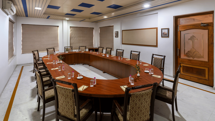 A conference room at Amantra Shilpi Resort, Udaipur features a large oval wooden table surrounded by chairs and wall panels.