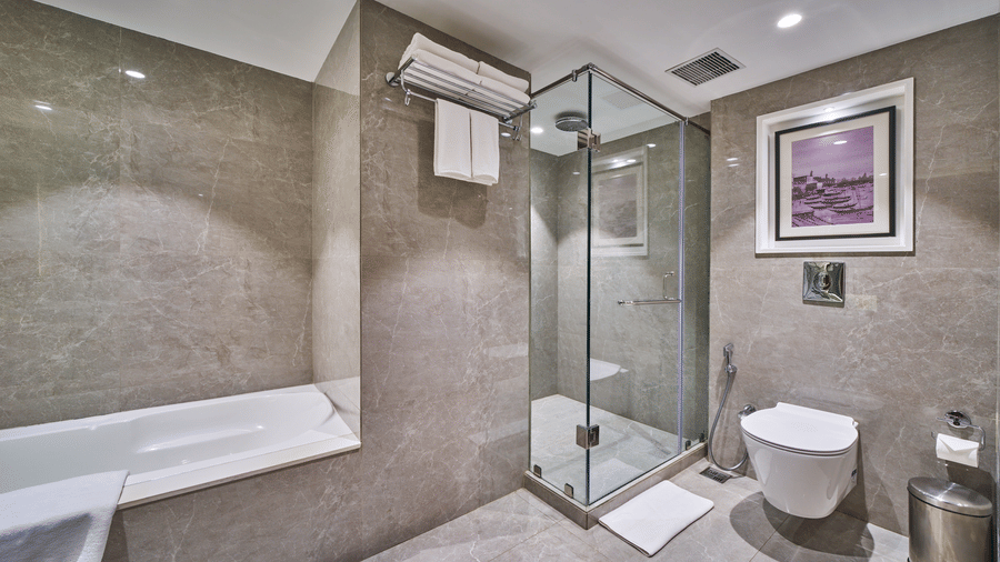 A bathroom featuring a white bathtub, a glass shower cubicle, and a wall-mounted toilet | HHI Varanasi