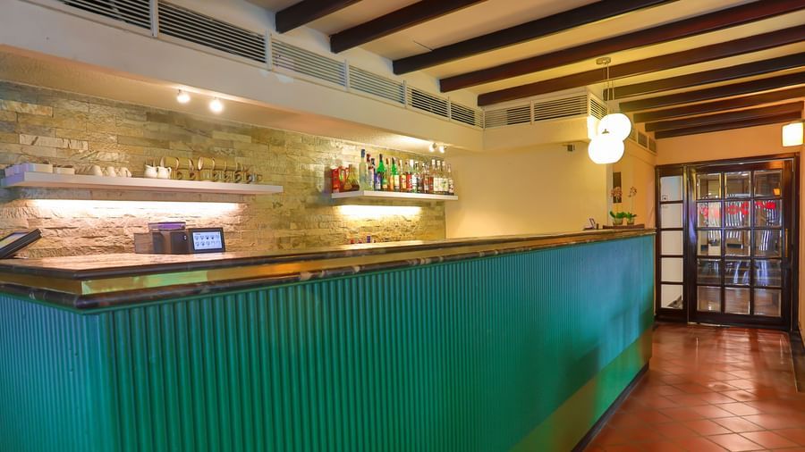 A long, ribbed counter with shelves of bottles and glasses behind it, and a doorway at the far end, at Shilton International, Kochi.