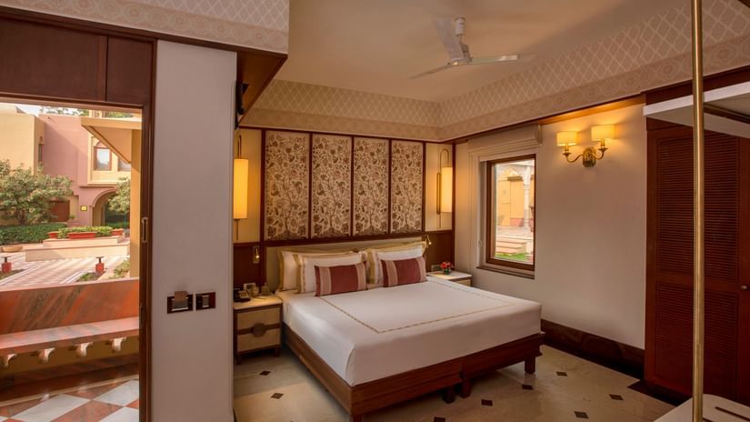 Luxurious bedroom with a king-sized bed, ornate headboard, elegant lighting, and an open balcony offering serene outdoor views