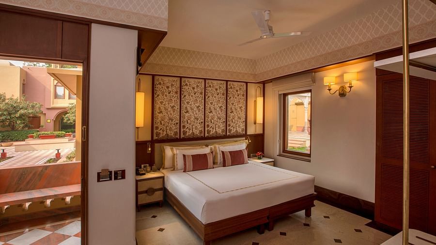 Luxurious bedroom with a king-sized bed, ornate headboard, elegant lighting, and an open balcony offering serene outdoor views