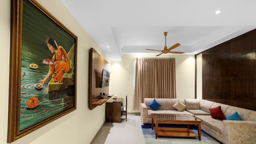 Living area at Inde Reva Resorts Rishhikesh with artwork on the wall, ceiling fan, and beige L-shaped sofa near curtains.
