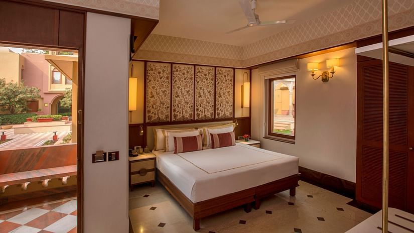 Luxurious bedroom with a king-sized bed, ornate headboard, elegant lighting, and an open balcony offering serene outdoor views