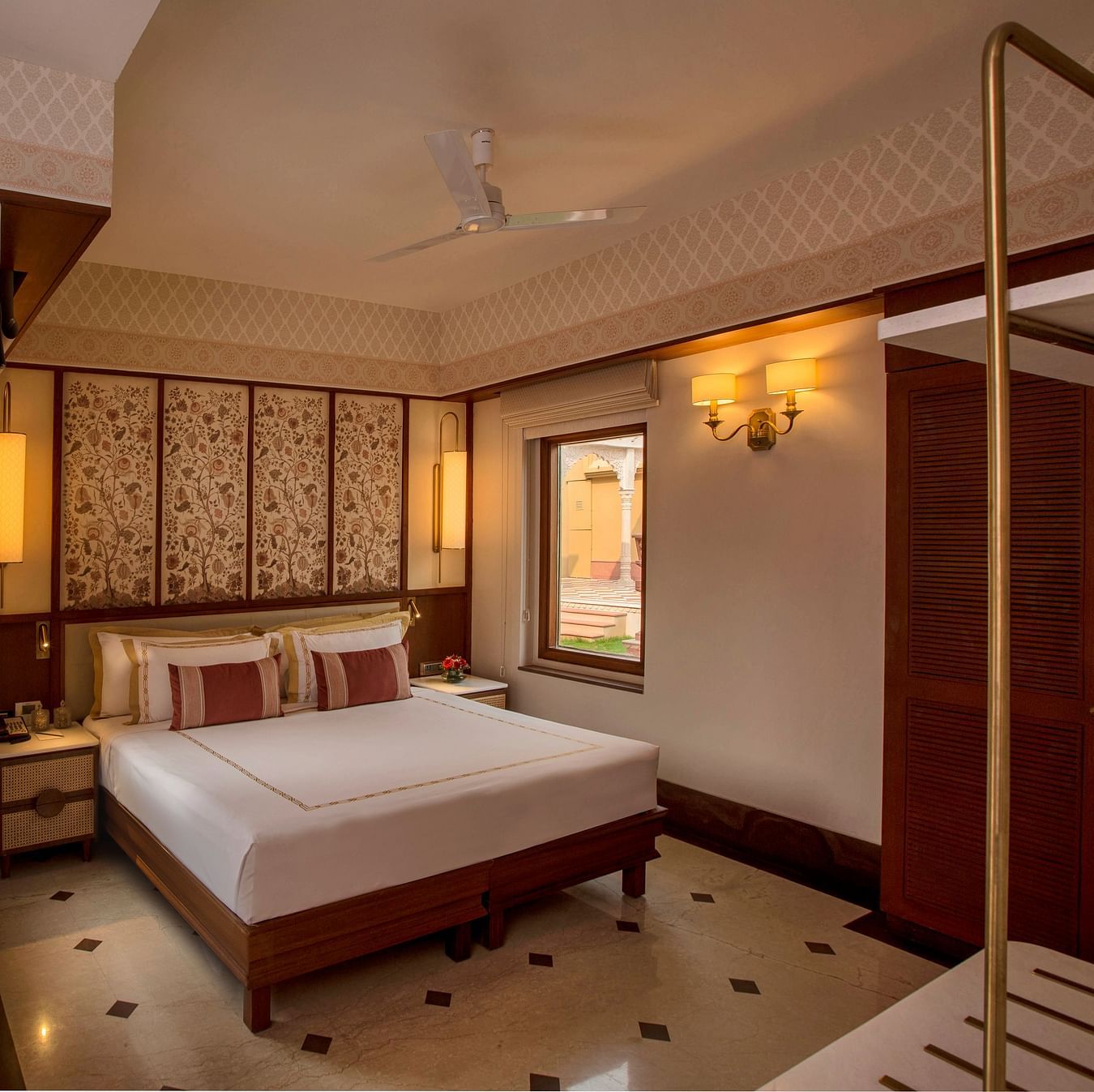 Luxurious bedroom with a king-sized bed, ornate headboard, elegant lighting, and an open balcony offering serene outdoor views