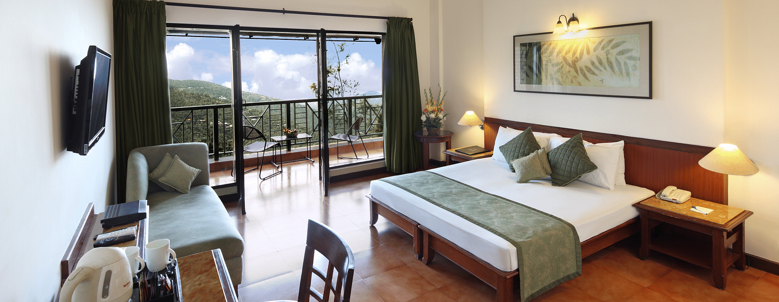 A bedroom featuring a study table and chair, a bedside table with a lamp, and a balcony offering a stunning mountain view -  Baikunth resort, kasauli 