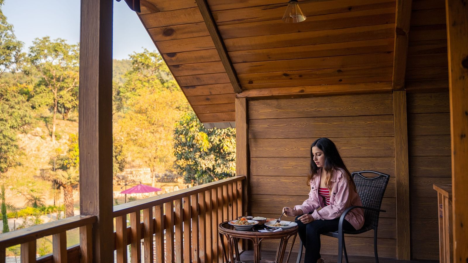 A woman enjoying breakfast at the balcony of Pinewood Cottage at the Sylvan Retreat, Dehradun.