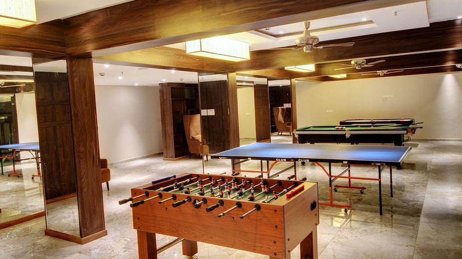 A recreational room featuring a table tennis table, a foosball table and a billiards table, with wooden beams overhead and polished marble floors.