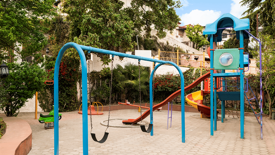 An outdoor play area featuring blue swings and a play structure with a slide at Ramada by Wyndham Mussoorie Mall Road.