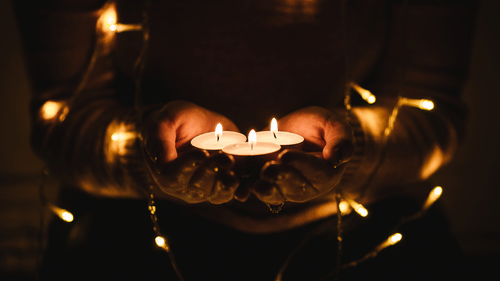 A person holding lit tea light candles in their hands.