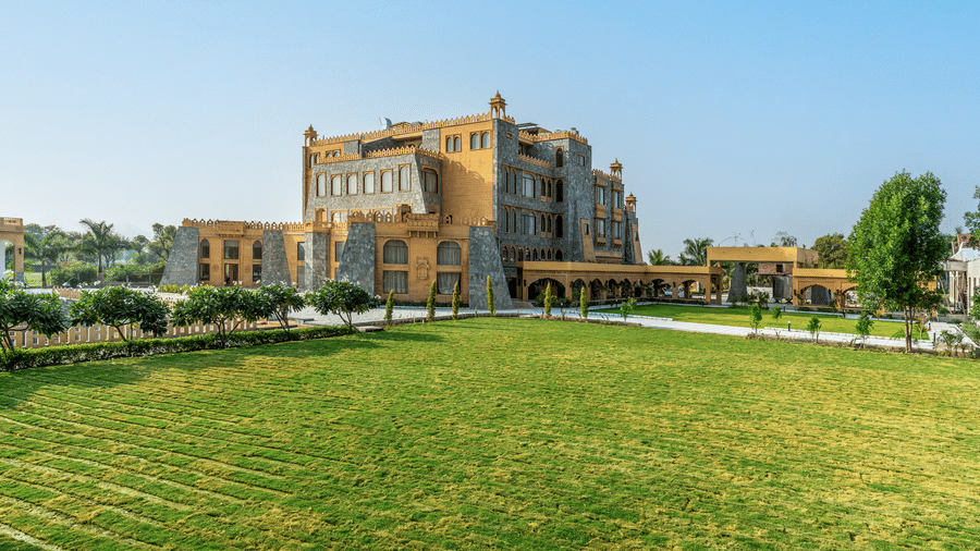 Wide shot of the EsthereaRaj Leela, Ranakpur's facade facing a large, manicured green lawn under a clear sky.