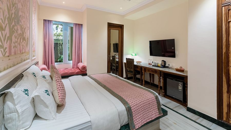 A spacious bedroom view from the headboard at Panna Vilas Palace, featuring a wall-mounted television above a wooden table, with large windows enhancing the light.