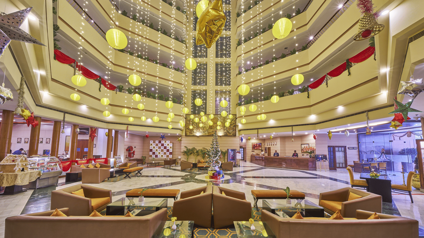 An indoor atrium lobby with yellow hanging lanterns, seating areas, and multiple floor balconies | HHI Varanasi