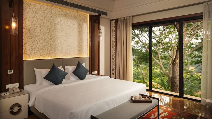Another view of a hotel bedroom with a similar setup, showcasing a large bed, bedside tables, and a window with an outdoor view.