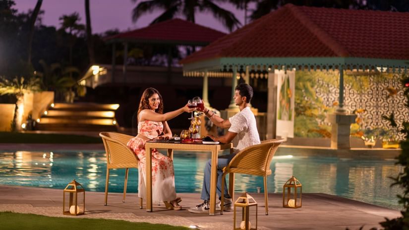 Couple enjoying a candlelit outdoor dinner beside a pool under twilight skies.