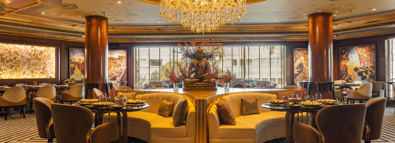 Erawaan dining at The Claridges New Delhi, featuring a chandelier, cosy sofas, and a serene Buddha statue centerpiece