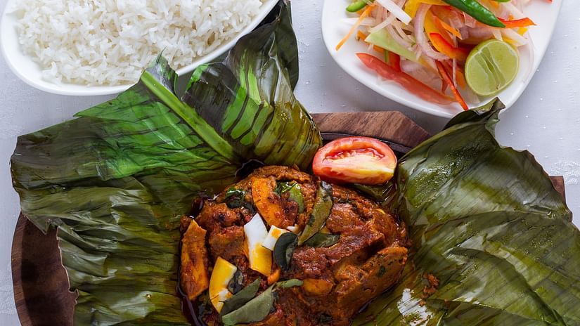 A meal served on a plate with rice, a curry served on a banana leaf, and a side of salad.