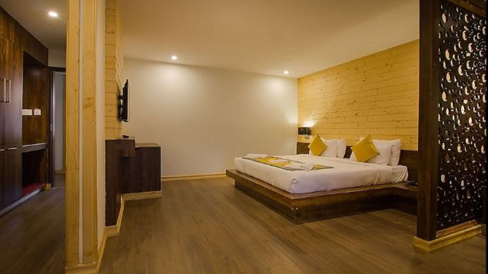 An image of an executive premium room with a bed, flat scree TV, a wooden panelled accent wall behind the bed, and the room is lit with warm lighting - Yashshree Sanderling, Darjeeling